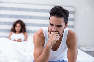 Tensed man sitting on bed while wife in background