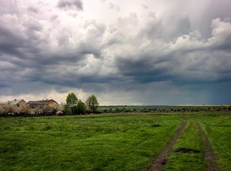 Fototapeta na wymiar Rainy storm clouds above green spring field and small village