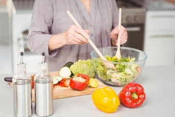 Fototapeta na wymiar Midsection of woman preparing salad while standing at kitchen counter