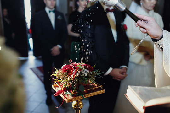 Priest sprinkles wedding rings on the red bouquet