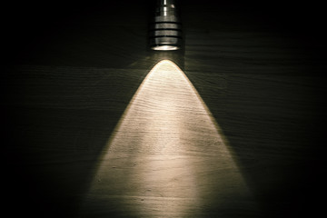 Flashlight and a beam of light in darkness. A modern led light with bright projection on dark wood table. Surface with copy space.