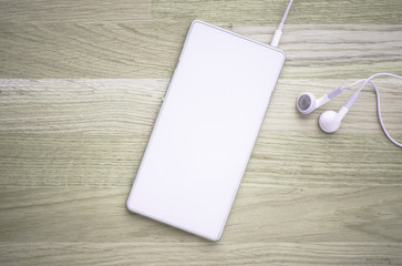 White cellphone and headphones lying on wooden table. Concept of audio, listening to music on the go or mobile accessory.