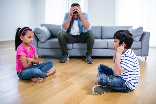 Annoyed father sitting on sofa while kids fighting 