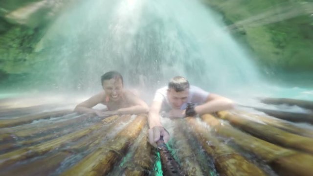 Couple of tourist experiencing a natural waterfall hydro message while lying down on a raft laughing so much.
