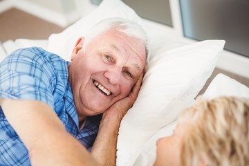 Portrait of happy man lying with wife on bed