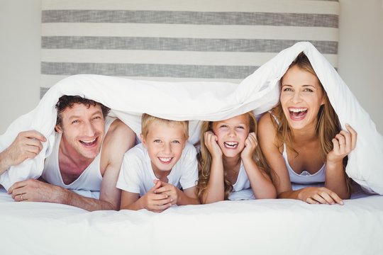 Portrait of family covered with duvet on bed