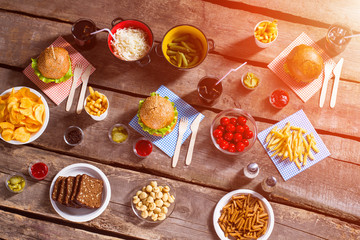 Burgers and pickles with tomatoes. Beverages and food on table. Cooked food with cool drinks. Weekend meal for guests.