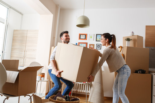 Young married couple carrying big cardboard box into new home. Moving house.	