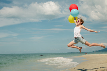 Teen girl with balloons jumping on the beach at the day time