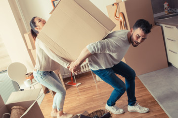 Young married couple carrying big cardboard box into new home. Moving house.	