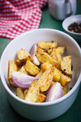 Oven-baked cut potato with red onion and Italian herbs, rustic, vintage or country style in a round bowl with red napkin on an old vintage green wooden background, closeup