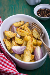 Oven-baked cut potato with red onion and Italian herbs, rustic, vintage or country style in a round bowl with red napkin on an old vintage green wooden background, closeup