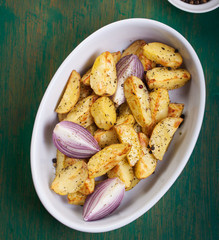 Oven-baked cut potato with red onion and Italian herbs, rustic, vintage or country style in a round...