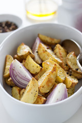 Oven-baked cut potato with red onion and Italian herbs, rustic, vintage or country style in a round bowl with white napkin on an old vintage wooden background, closeup