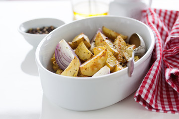 Oven-baked cut potato with red onion and Italian herbs, rustic, vintage or country style in a round...