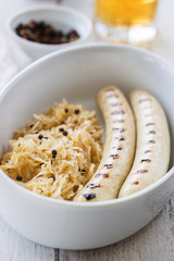 White grilled sausages with sauerkraut or cabbage, black pepper and fresh cold beer in a bowl on an old vintage wooden background, closeup