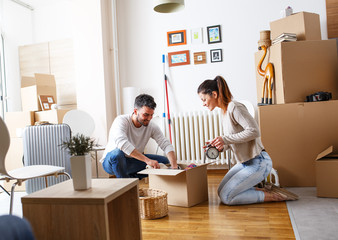 Young married couple moving into new home. They're unpacking card boxes with their accessories.