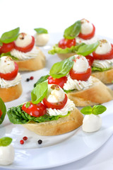 Käsehäppchen mit Tomate und Mozzarella, mit Basilikum und Frischkäse auf Baguette mit Romana-Salat angerichtet - Canapes with tomato, mozzarella, olive oil, balsamic vinegar and basil