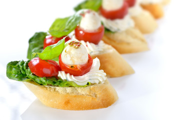 Käsehäppchen mit Tomate und Mozzarella, mit Basilikum und Frischkäse auf Baguette mit Romana-Salat angerichtet - Canapes with tomato, mozzarella, olive oil, balsamic vinegar and basil