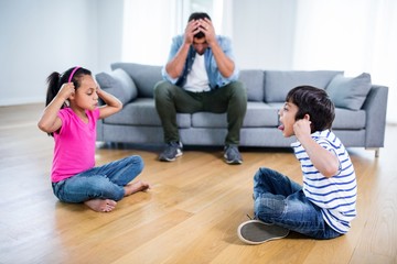 Annoyed father sitting on sofa while kids fighting 