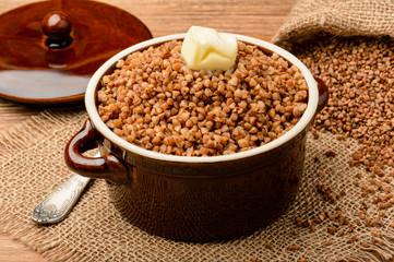 Boiled buckwheat porridge in ceramic pot on wooden background.