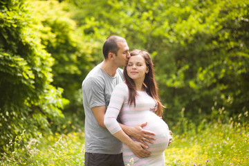 Happy couple waiting for baby. Man kisses pregnant woman and hugs her belly outdoors in summer, New family concept. Paternity.