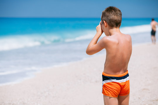 Beach vacation dream. Handsome young boy enjoying in beautiful tropical beach and taking some photos with his camera.