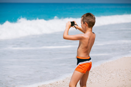 Beach vacation dream. Handsome young boy enjoying in beautiful tropical beach and taking some photos with his camera.