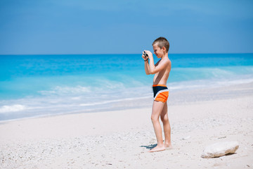 Beach vacation dream. Handsome young boy enjoying in beautiful tropical beach and taking some photos with his camera.