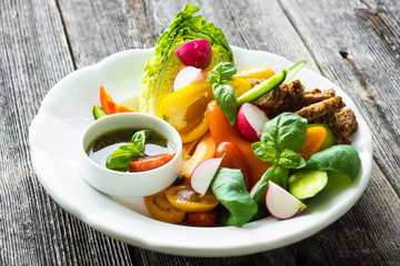 Delicious fresh sliced organic vegetables with homemade pesto on the plate and on the wooden background