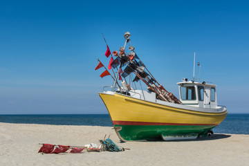 Small, colorful fishing boat in reggae colors on baltic beach, against radiant blue sky.