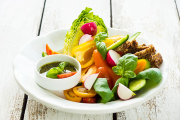 Delicious fresh sliced organic vegetables with homemade pesto on the plate and on the wooden background