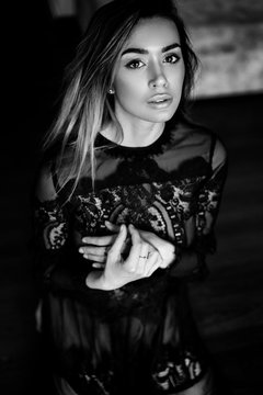 Black and white art photo. Beautiful, sexy, elegant woman with long blond hair posing in a black lace dress with make-up and hair style at home
