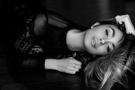 Black and white art photo. Beautiful, sexy, elegant woman with long blond hair posing in a black lace dress with make-up and hair style at home