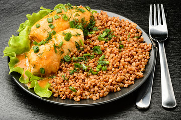 Stuffed meat rolls with tomato sauce and buckwheat on black plate.