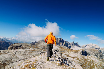 The guy in the orange jacket and sneakers running trails in the mountains. Dolomite, Alps