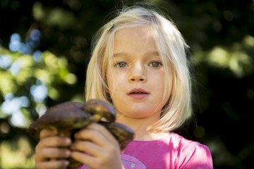 Child blond girl holding fresh mushrooms
