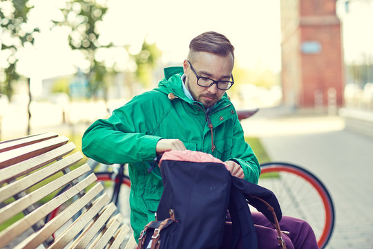 hipster man with backpack sitting on city bench