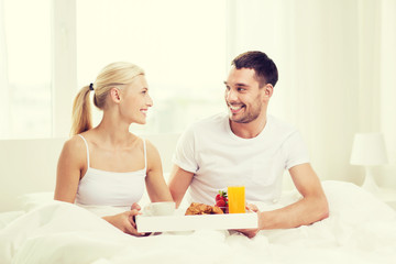 Obraz na płótnie Canvas happy couple having breakfast in bed at home