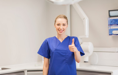 happy female dentist showing thumbs up at clinic - obrazy, fototapety, plakaty
