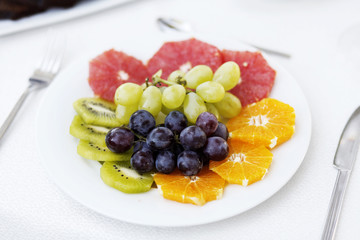 Plate of fruits, kiwi, orange , grapes on a table with knife and fork
