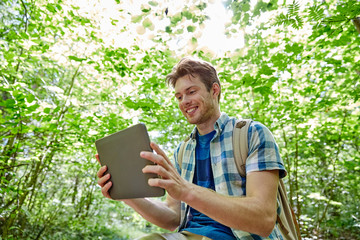 happy man with backpack and tablet pc in woods