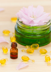 gold capsules of natural cosmetik for face, a little bottle with essential oil and rose on the wooden