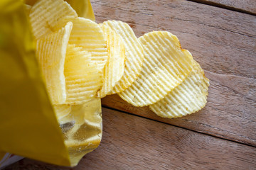 Opened pack with potato chips over wooden table