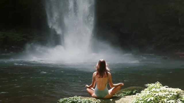 girl meditating in front of waterfall