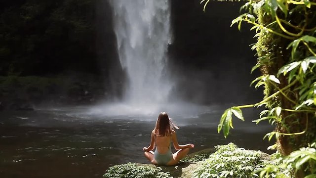 girl meditating in front of waterfall