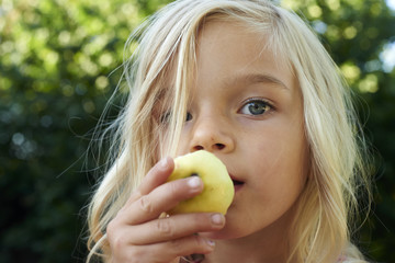 Portrait of the beautiful blond girl eating an apple outdoors