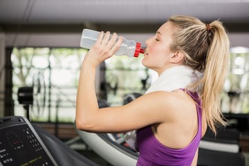 Woman on treadmill drinking water at gym