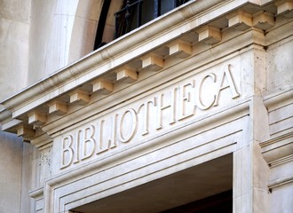 Close up of the entrance of a historic white stone library building in the Neoclassical style. An inscription over the doorway reads Bibliotheca, the Latin for Library.