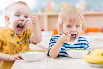 Funny little kids eating from plates in kindergarten